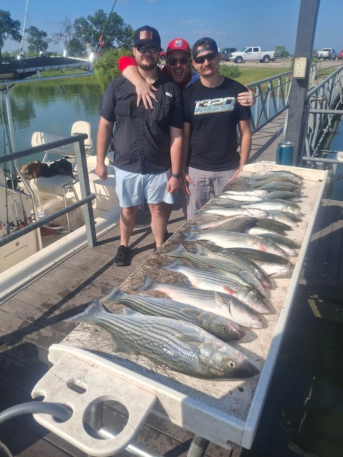 Three guys posing behind a full cleaning table of stripers at the dock